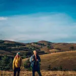 Portrait of a happy couple following trail along grassy mountain ridge and having fun together while walking a Camino