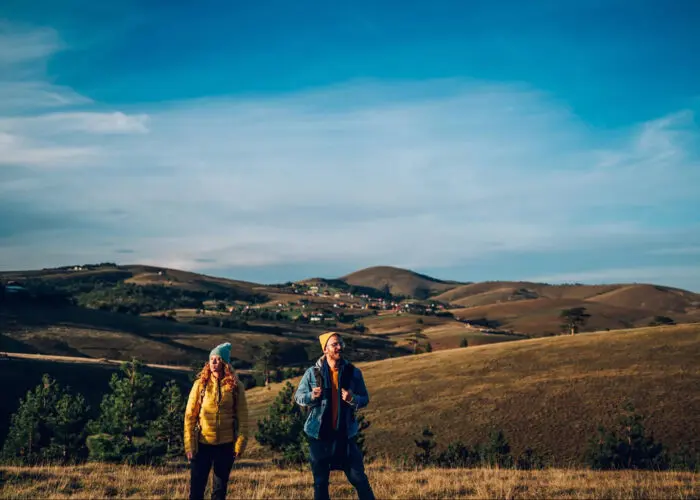 Portrait of a happy couple following trail along grassy mountain ridge and having fun together while walking a Camino